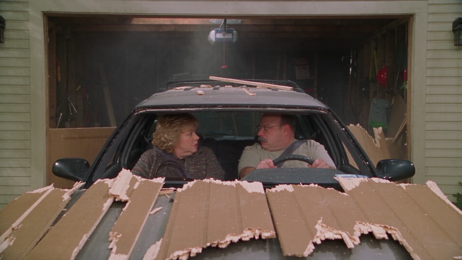 Gary und Linda sitzen im Auto, das rückwärts durch das Garagentor gekracht ist, zersplitterte Bretter liegen auf der Motorhaube